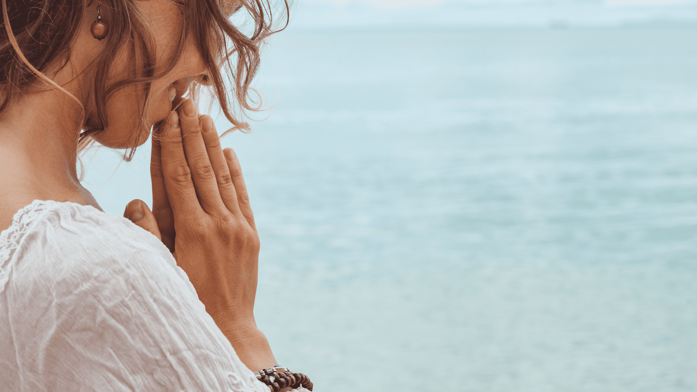 Woman praying beside the ocean, representing trust, surrender, and connection with the water element