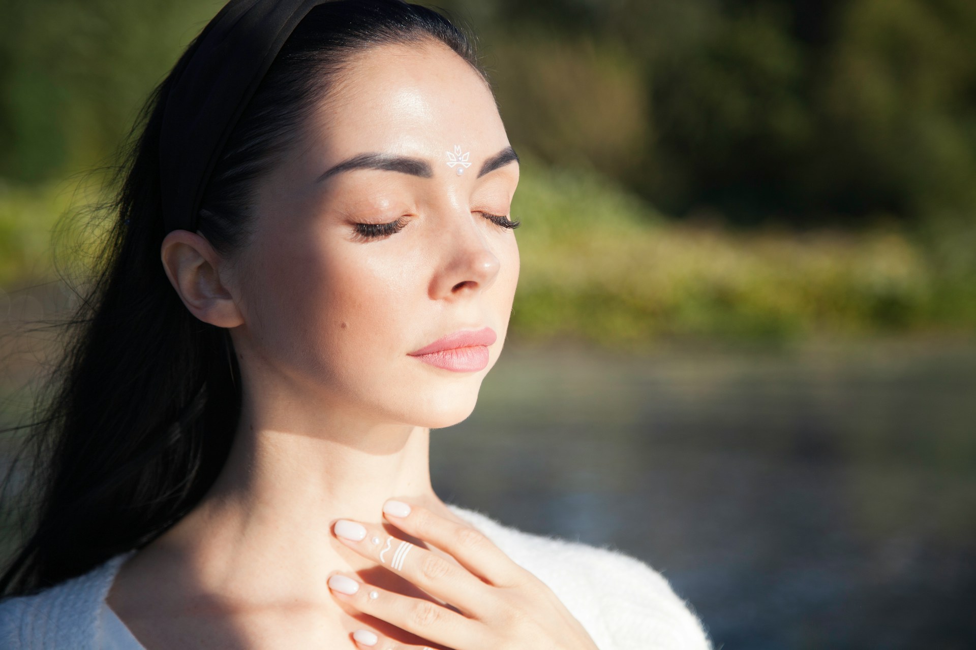 Woman gently touching her throat by a bright window, representing the early signs of Light Language activation and intuitive awakening.